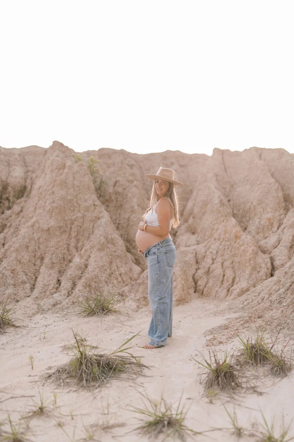 Hailey Aliff standing in soft evening light among desert ridges, hands resting on her pregnant belly