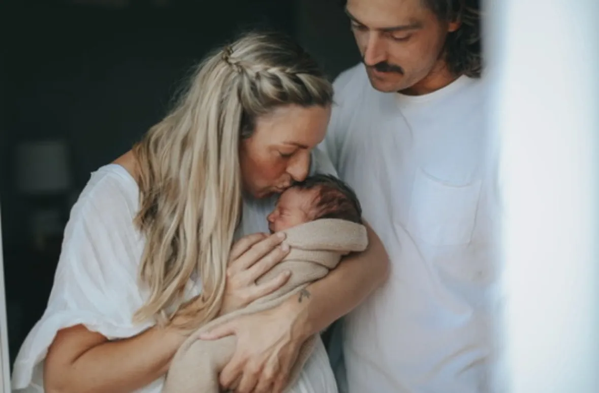 A father tenderly kissing his newborn's forehead while the mother holds the baby